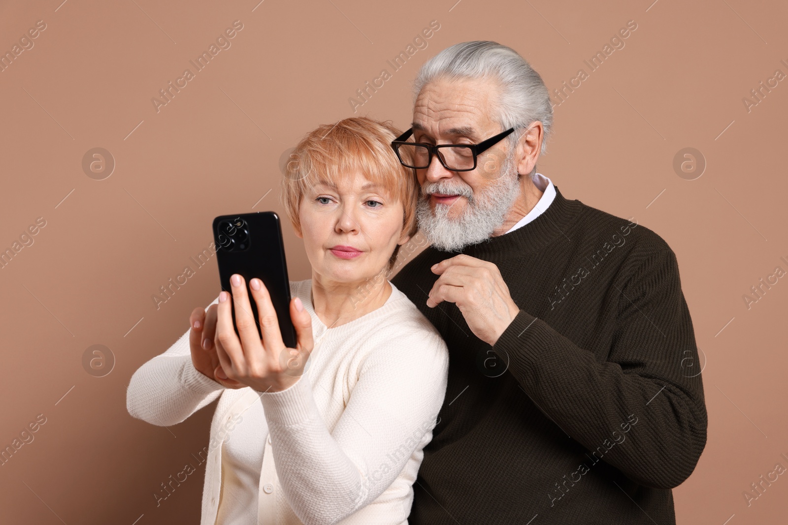 Photo of Lovely senior couple looking at smartphone on beige background