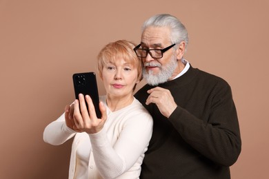 Lovely senior couple looking at smartphone on beige background