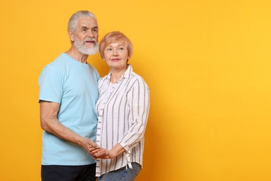 Photo of Lovely senior couple holding hands on orange background. Space for text