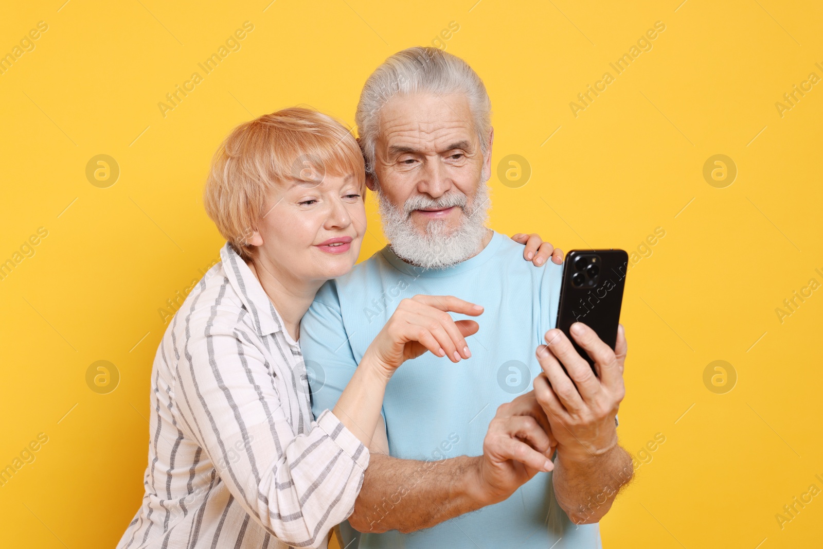 Photo of Lovely senior couple looking at smartphone on orange background