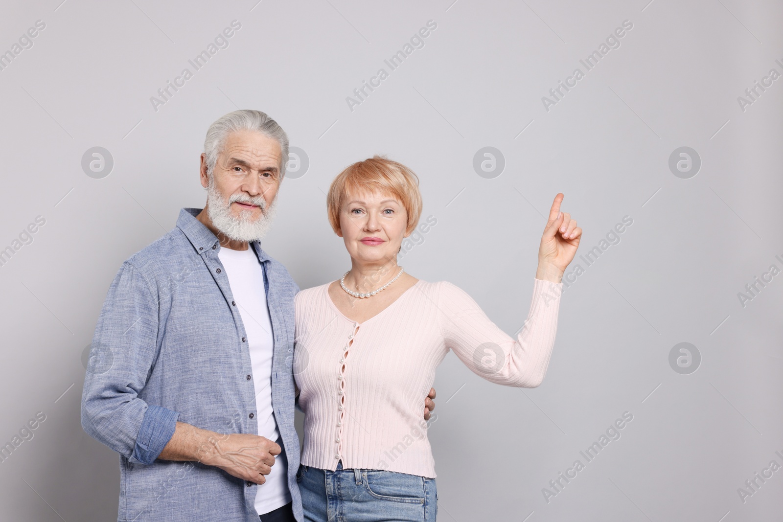 Photo of Lovely senior couple. Woman pointing at something on grey background. Space for text