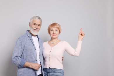 Lovely senior couple. Woman pointing at something on grey background. Space for text