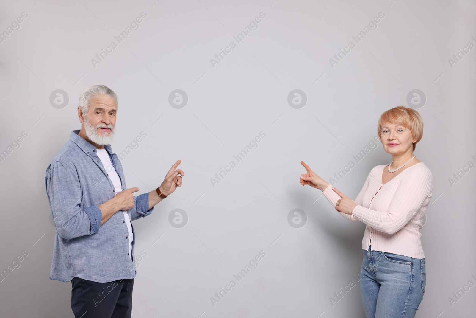 Photo of Lovely senior couple pointing at something on grey background. Space for text