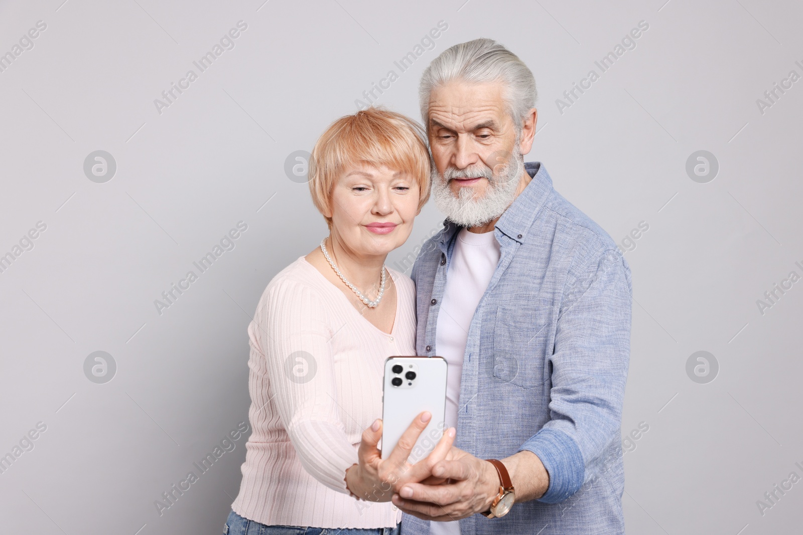 Photo of Lovely senior couple looking at smartphone on grey background