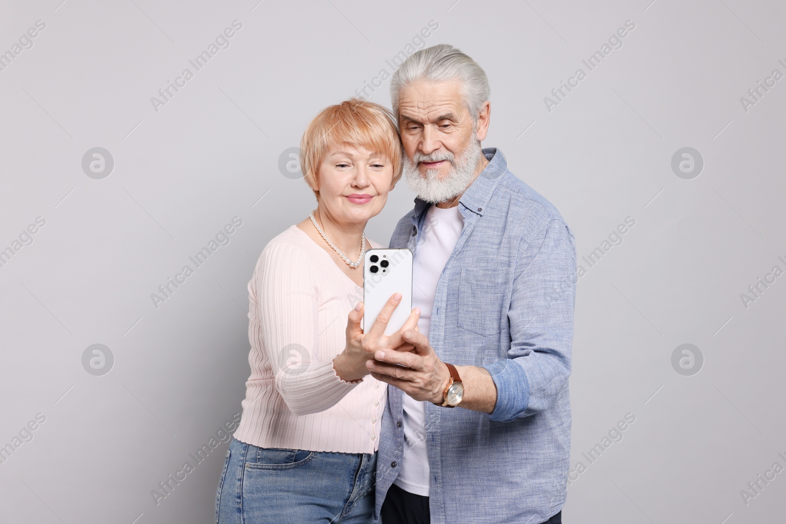 Photo of Lovely senior couple looking at smartphone on grey background