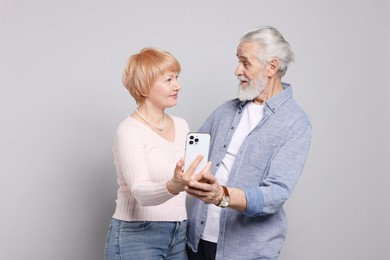 Photo of Lovely senior couple with smartphone on grey background