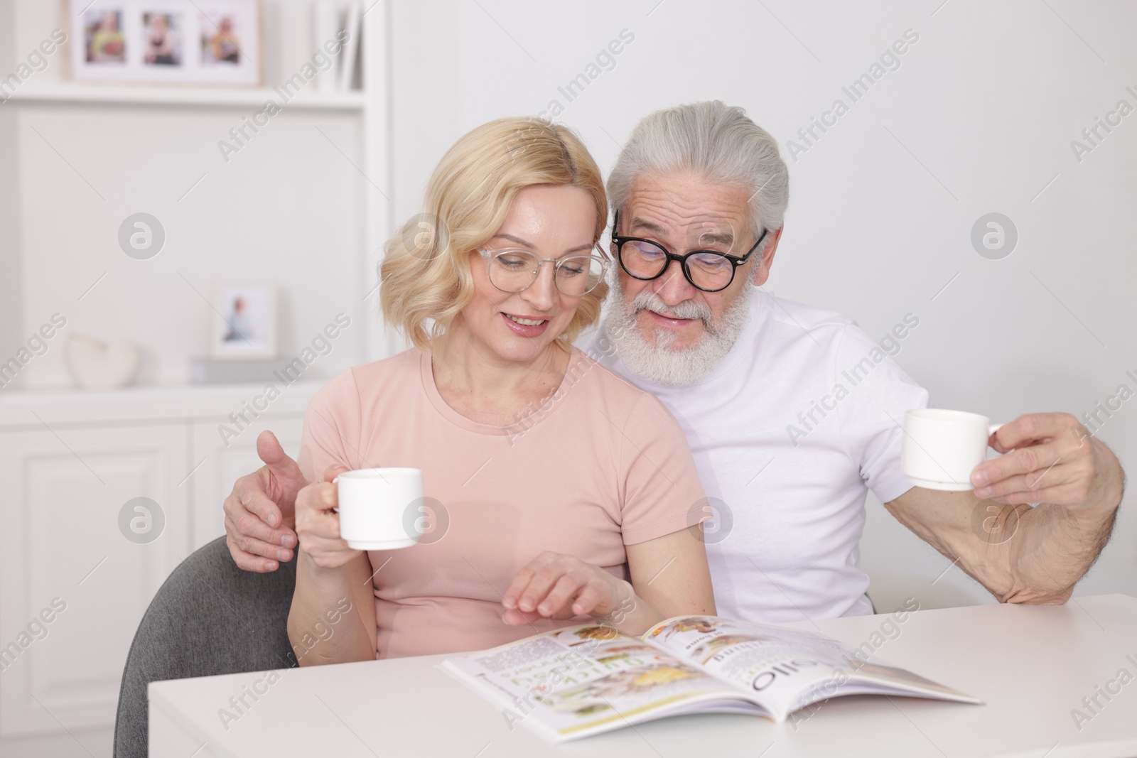 Photo of Senior man and mature woman with coffee reading magazine at home. Happy couple