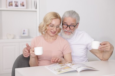 Photo of Senior man and mature woman with coffee reading magazine at home. Happy couple