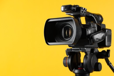 Photo of Modern video camera on yellow background, closeup. Space for text