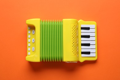 Photo of Toy accordion on orange background, top view. Child's musical instrument