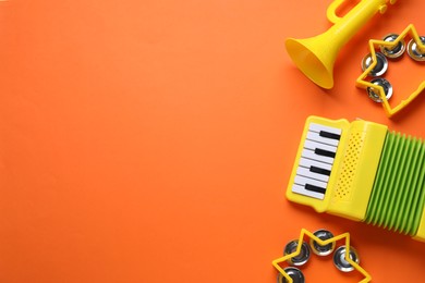 Photo of Bright toy tambourines, accordion and horn on orange background, flat lay. Space for text