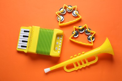 Photo of Bright toy tambourines, accordion and horn on orange background, flat lay