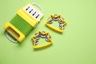 Photo of Bright toy tambourines and accordion on green background, flat lay. Space for text