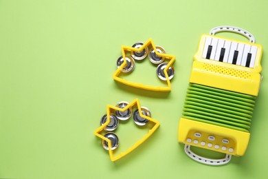 Photo of Bright toy tambourines and accordion on green background, flat lay. Space for text