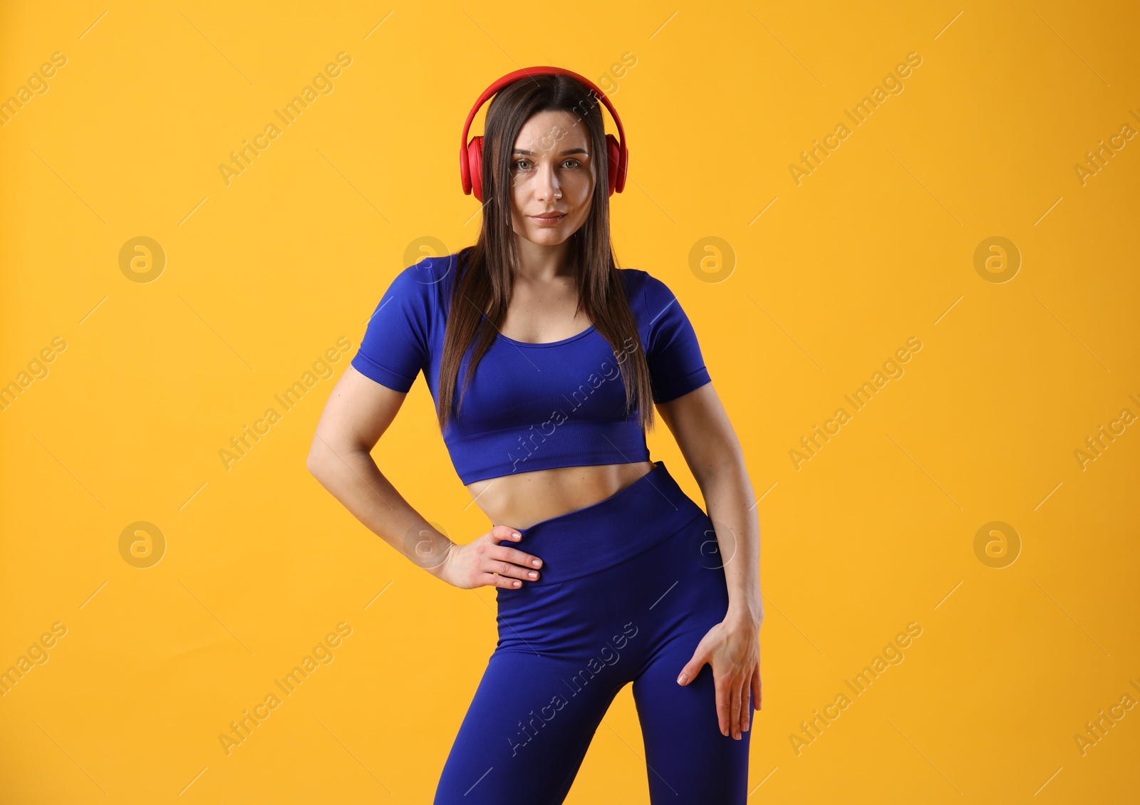 Photo of Woman in sportswear with headphones posing on orange background