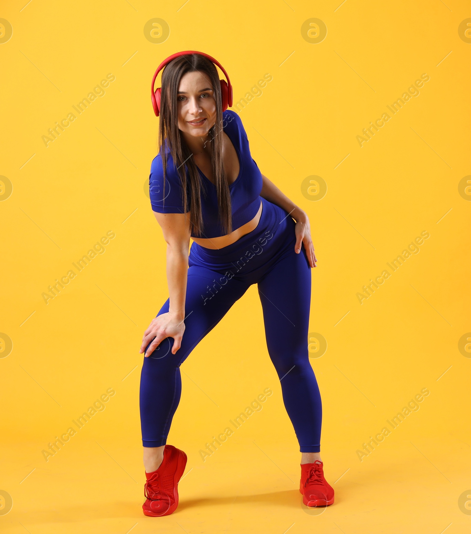 Photo of Woman in sportswear with headphones posing on orange background