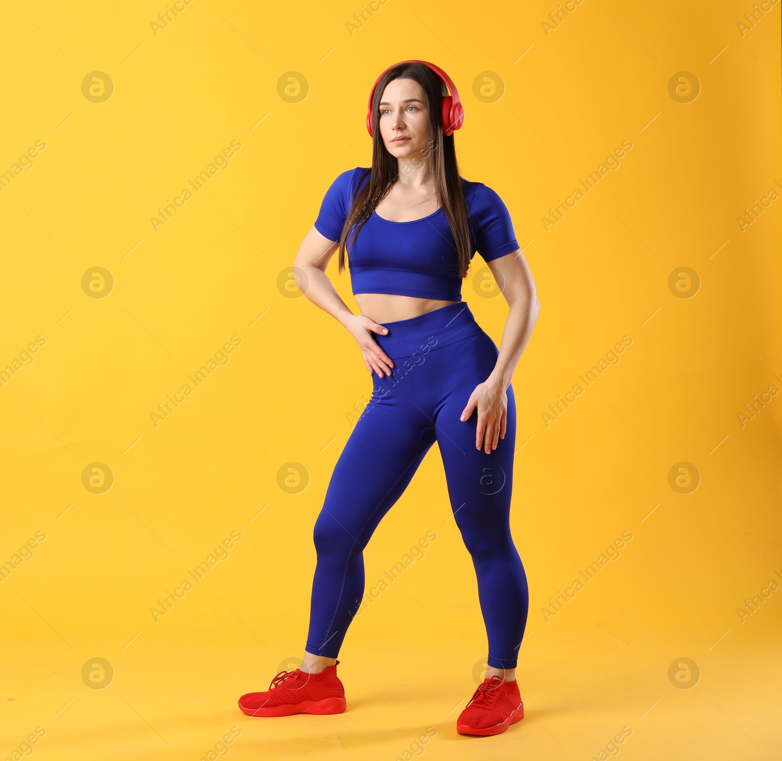 Photo of Woman in sportswear with headphones posing on orange background