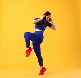 Woman in sportswear with headphones posing on orange background