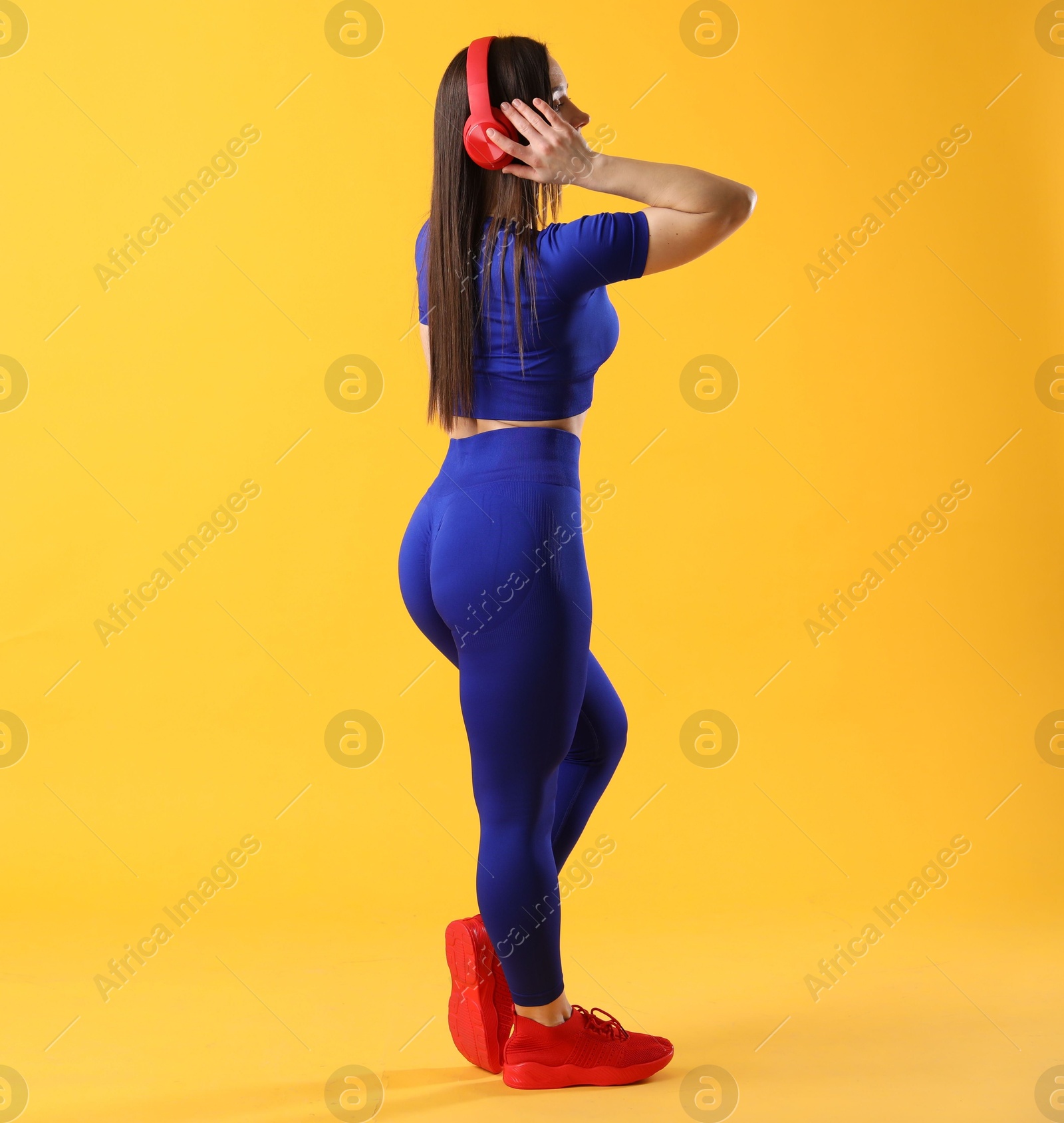 Photo of Woman in sportswear with headphones posing on orange background