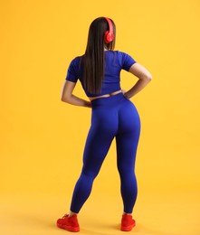 Photo of Woman in sportswear with headphones posing on orange background, back view