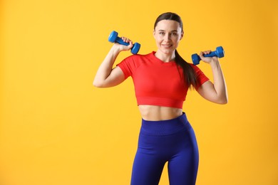 Photo of Woman in sportswear exercising with dumbbells on orange background, space for text