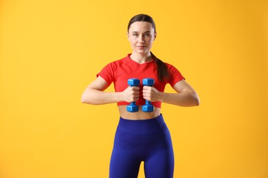 Woman in sportswear exercising with dumbbells on orange background