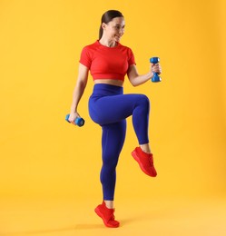 Photo of Woman in sportswear exercising with dumbbells on orange background