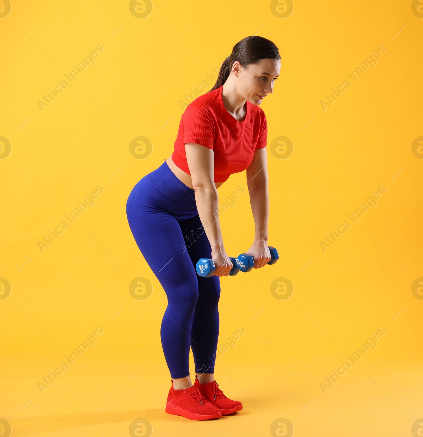 Photo of Woman in sportswear exercising with dumbbells on orange background