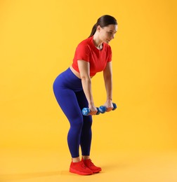 Woman in sportswear exercising with dumbbells on orange background