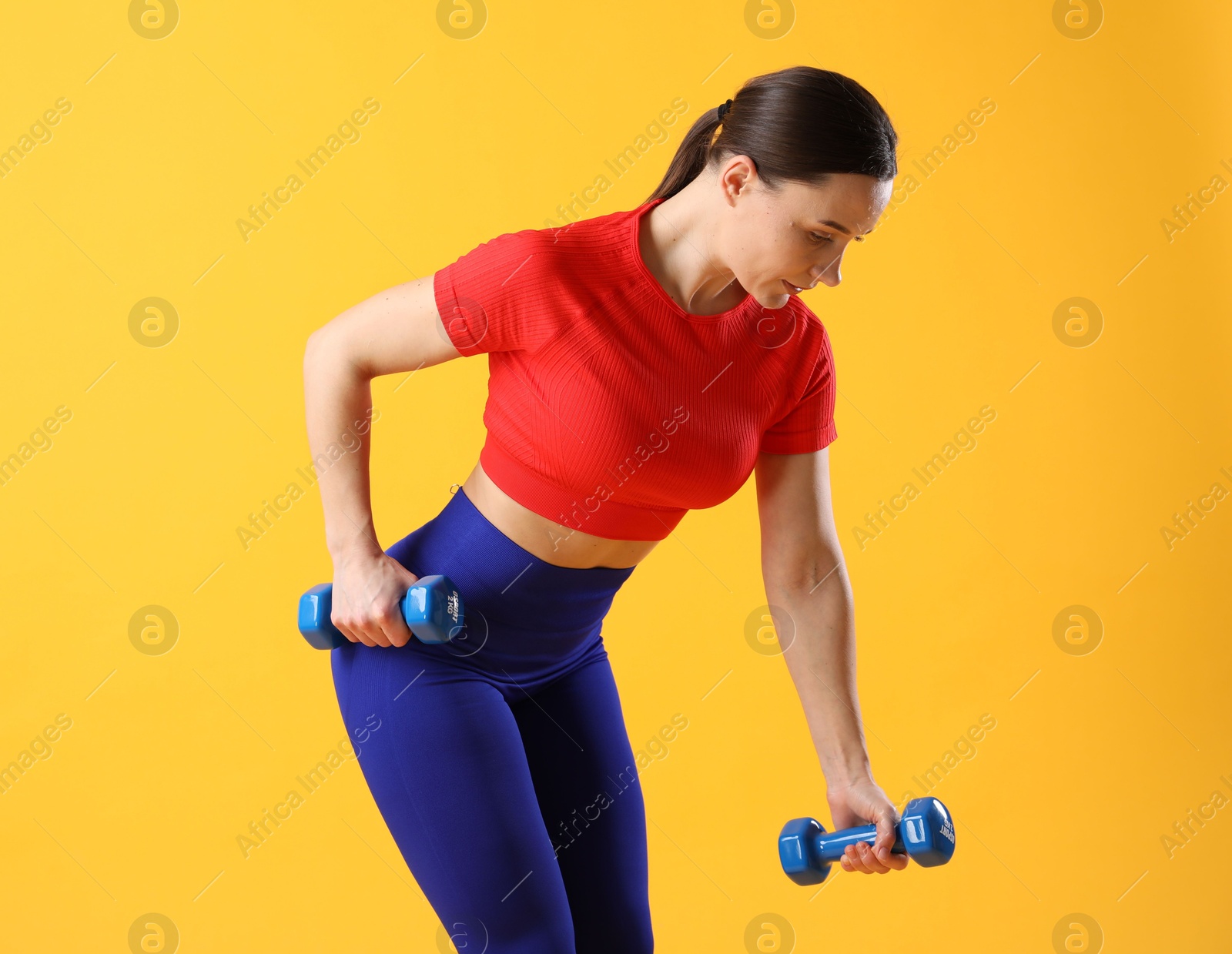 Photo of Woman in sportswear exercising with dumbbells on orange background