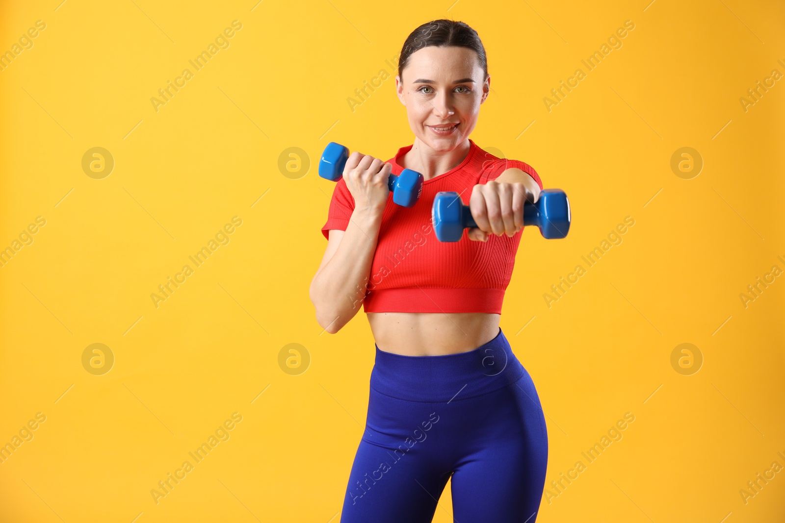 Photo of Woman in sportswear exercising with dumbbells on orange background, space for text