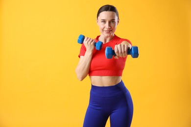 Woman in sportswear exercising with dumbbells on orange background, space for text