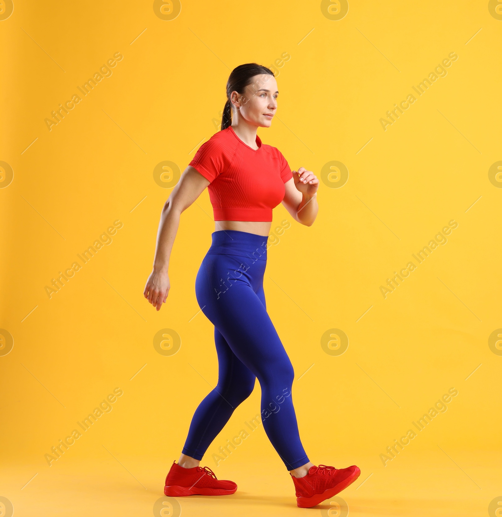 Photo of Woman in sportswear walking on orange background