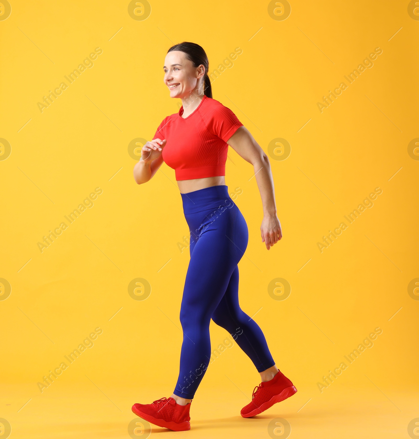 Photo of Woman in sportswear walking on orange background