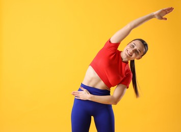 Woman in sportswear exercising on orange background, space for text