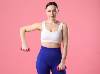 Photo of Woman in sportswear exercising with dumbbells on pink background