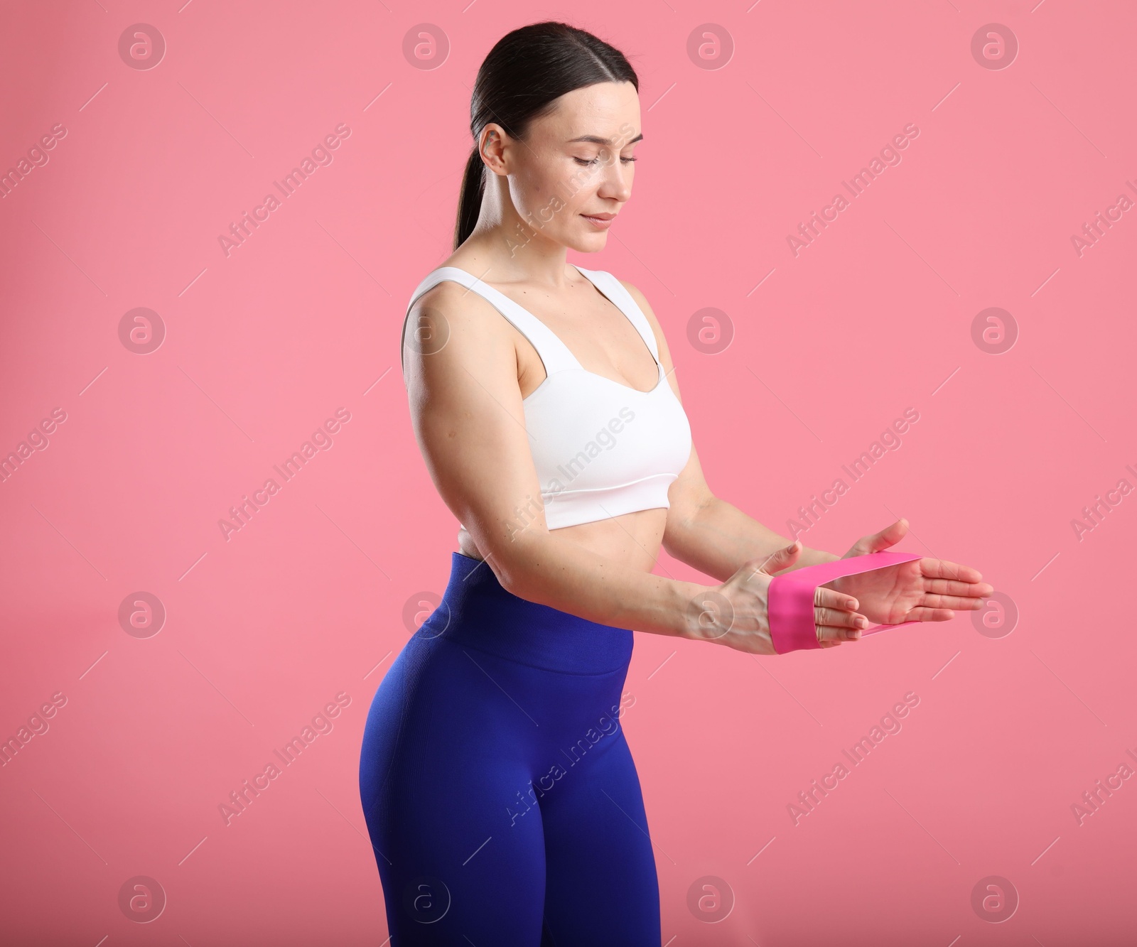 Photo of Woman in sportswear exercising with elastic band on pink background