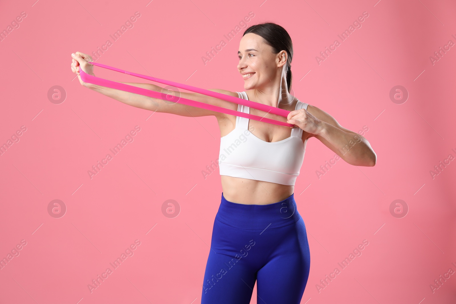 Photo of Woman in sportswear exercising with elastic band on pink background