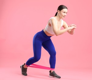 Photo of Woman in sportswear exercising with elastic band on pink background