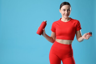 Woman in sportswear with water bottle on light blue background, space for text