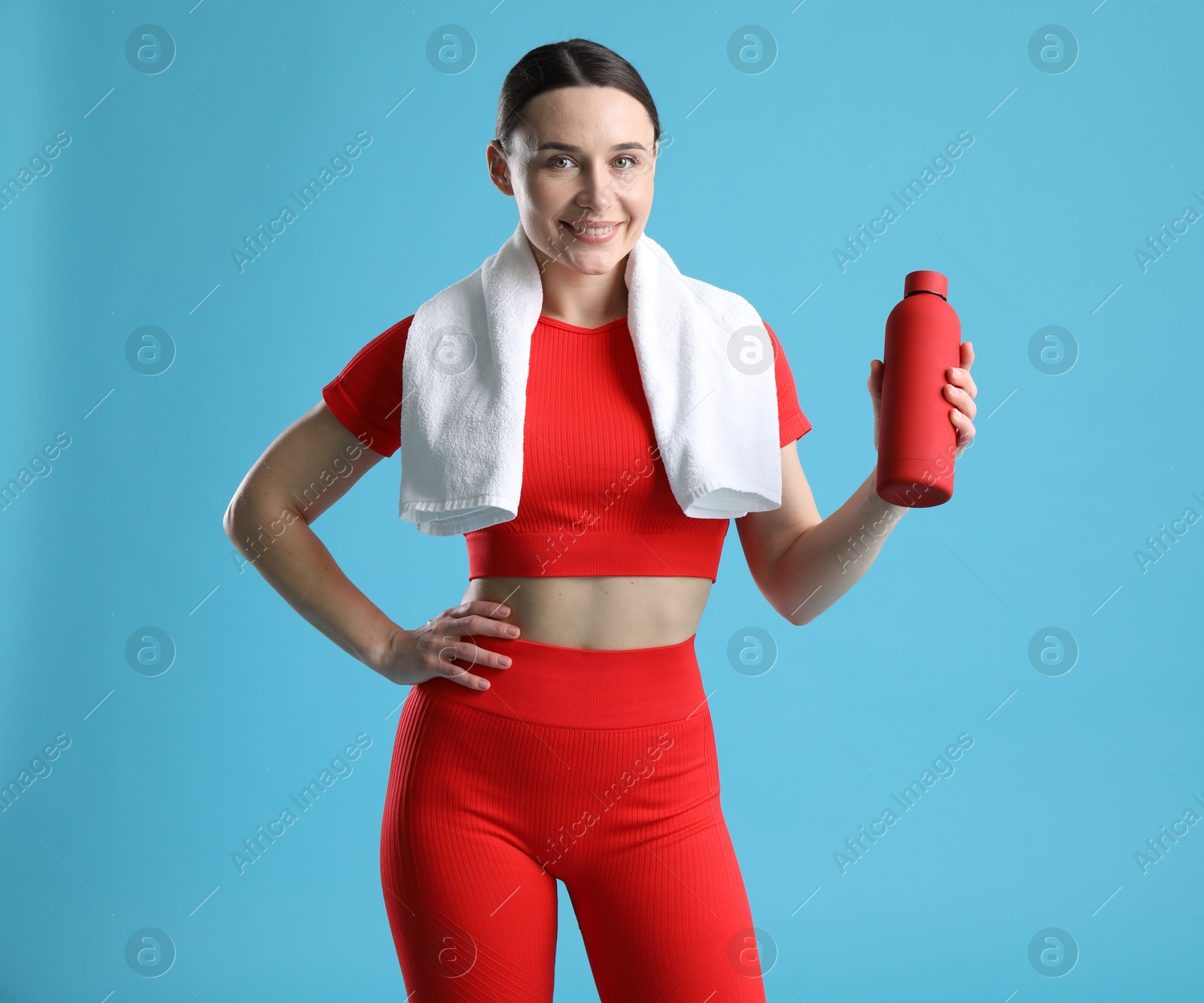 Photo of Woman in sportswear with water bottle and towel on light blue background