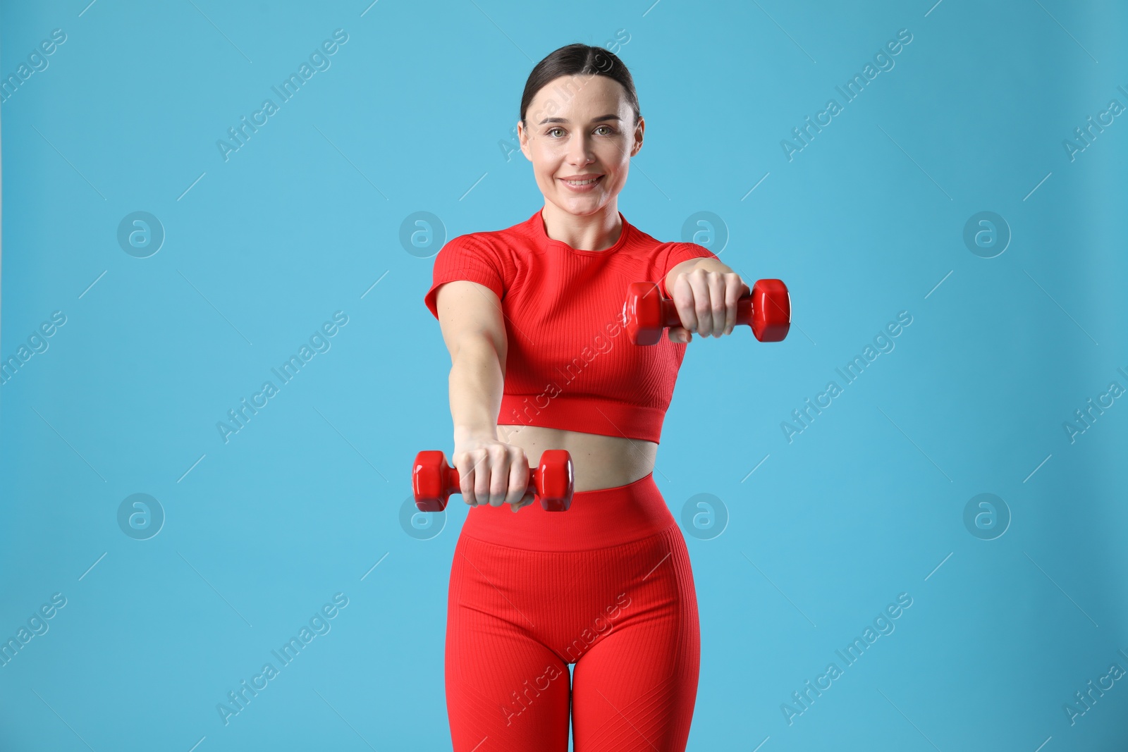 Photo of Woman in sportswear exercising with dumbbells on light blue background