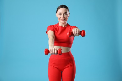 Photo of Woman in sportswear exercising with dumbbells on light blue background