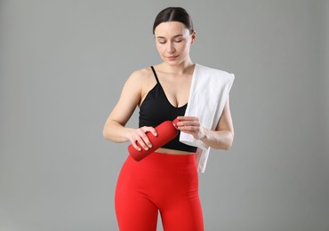 Woman in sportswear with water bottle and towel on grey background