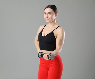 Photo of Woman in sportswear exercising with dumbbell on grey background