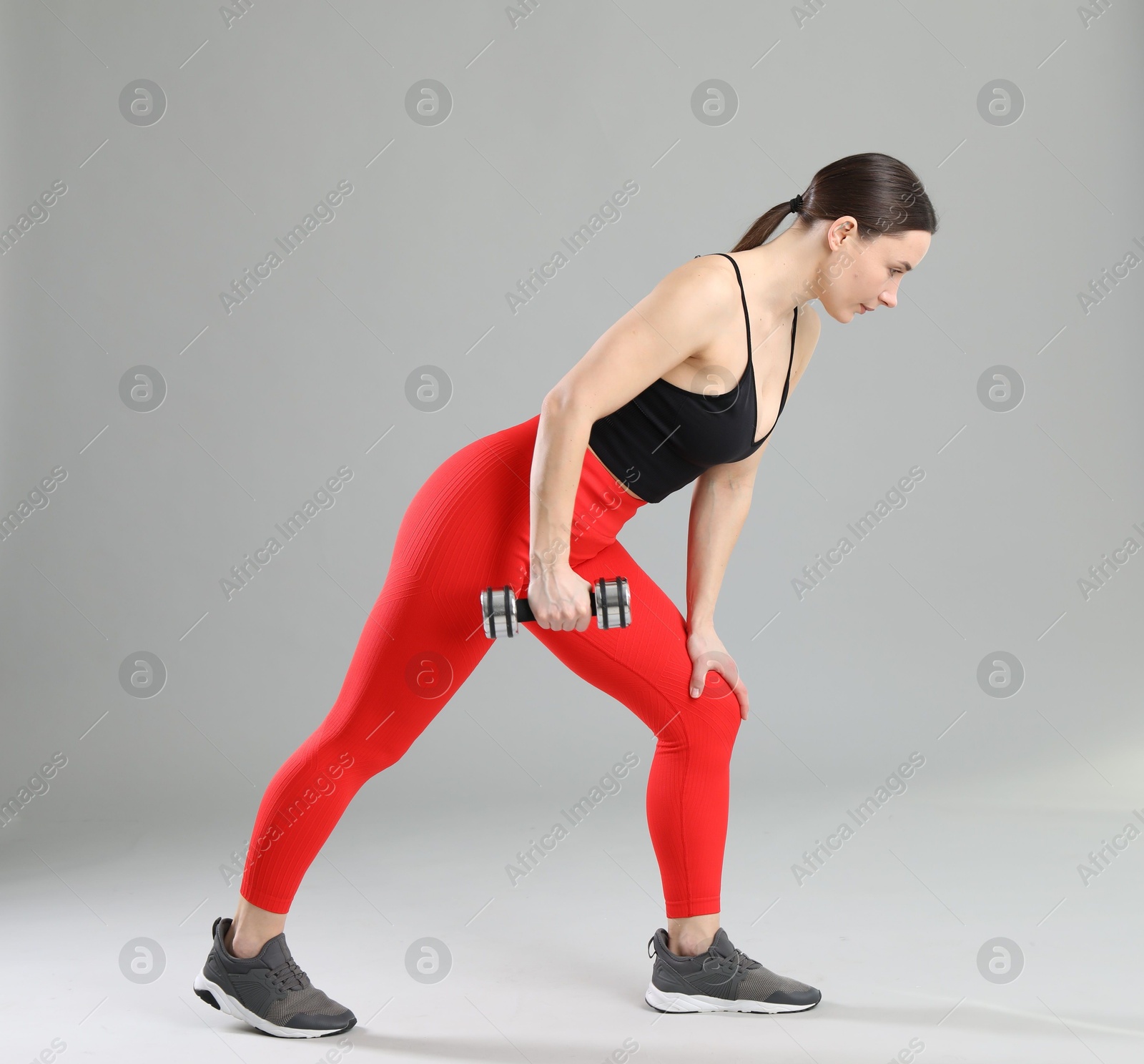 Photo of Woman in sportswear exercising with dumbbell on grey background