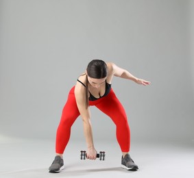 Photo of Woman in sportswear exercising with dumbbell on grey background