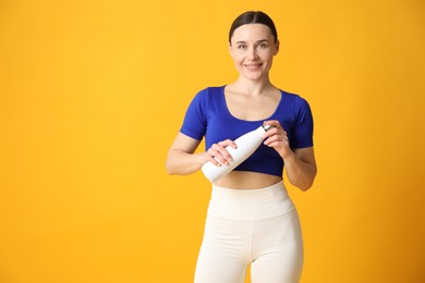 Photo of Woman in stylish sportswear with water bottle on orange background, space for text