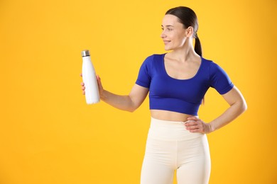 Photo of Woman in stylish sportswear with water bottle on orange background, space for text