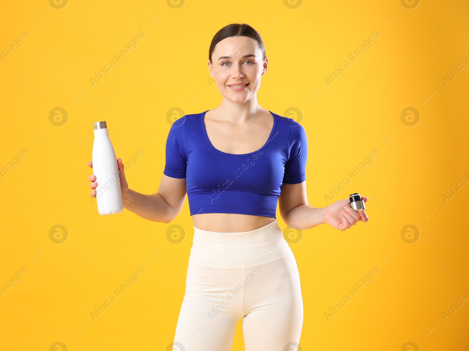 Photo of Woman in stylish sportswear with water bottle on orange background